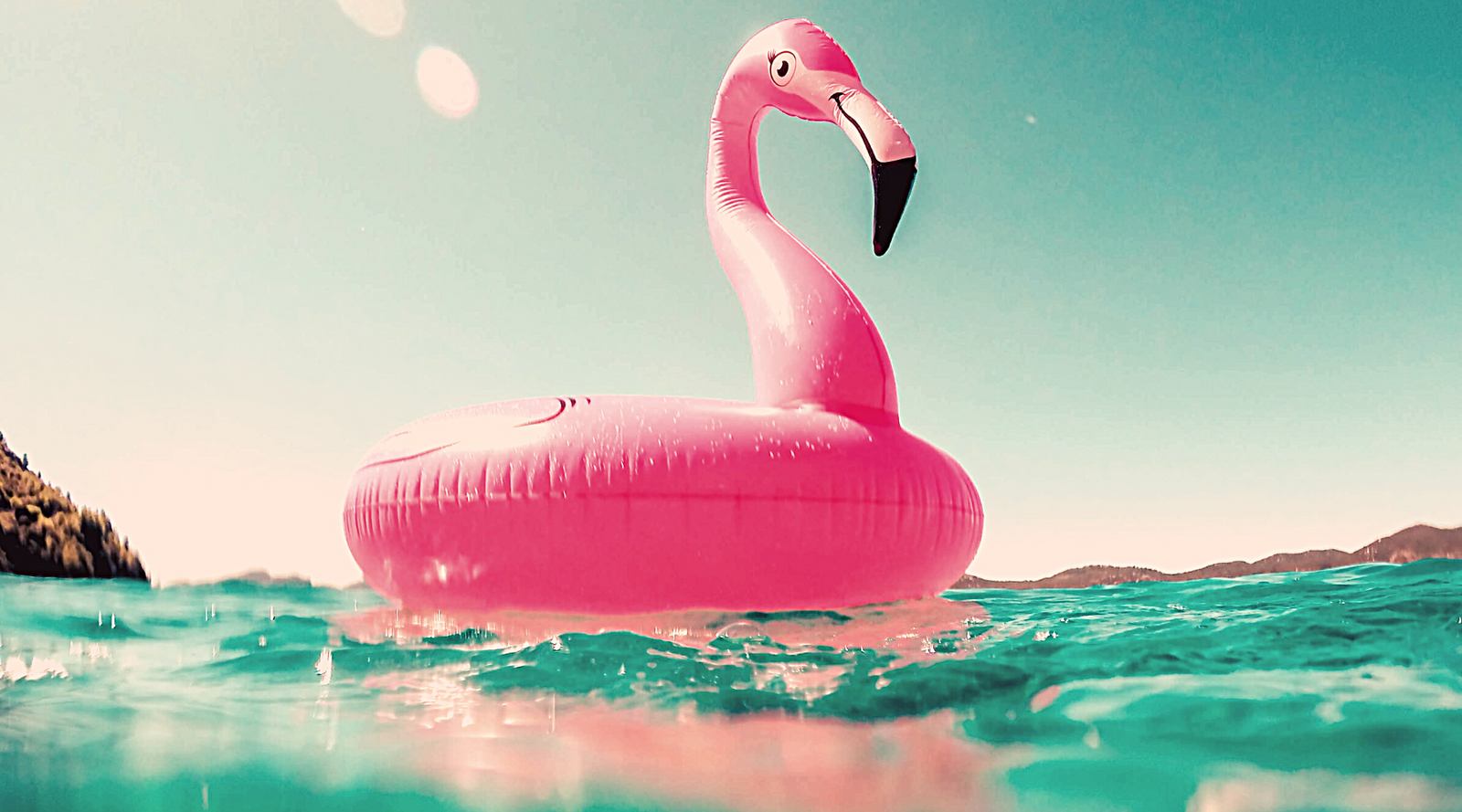 Pink flamingo raft floating on blue water with sky in background.