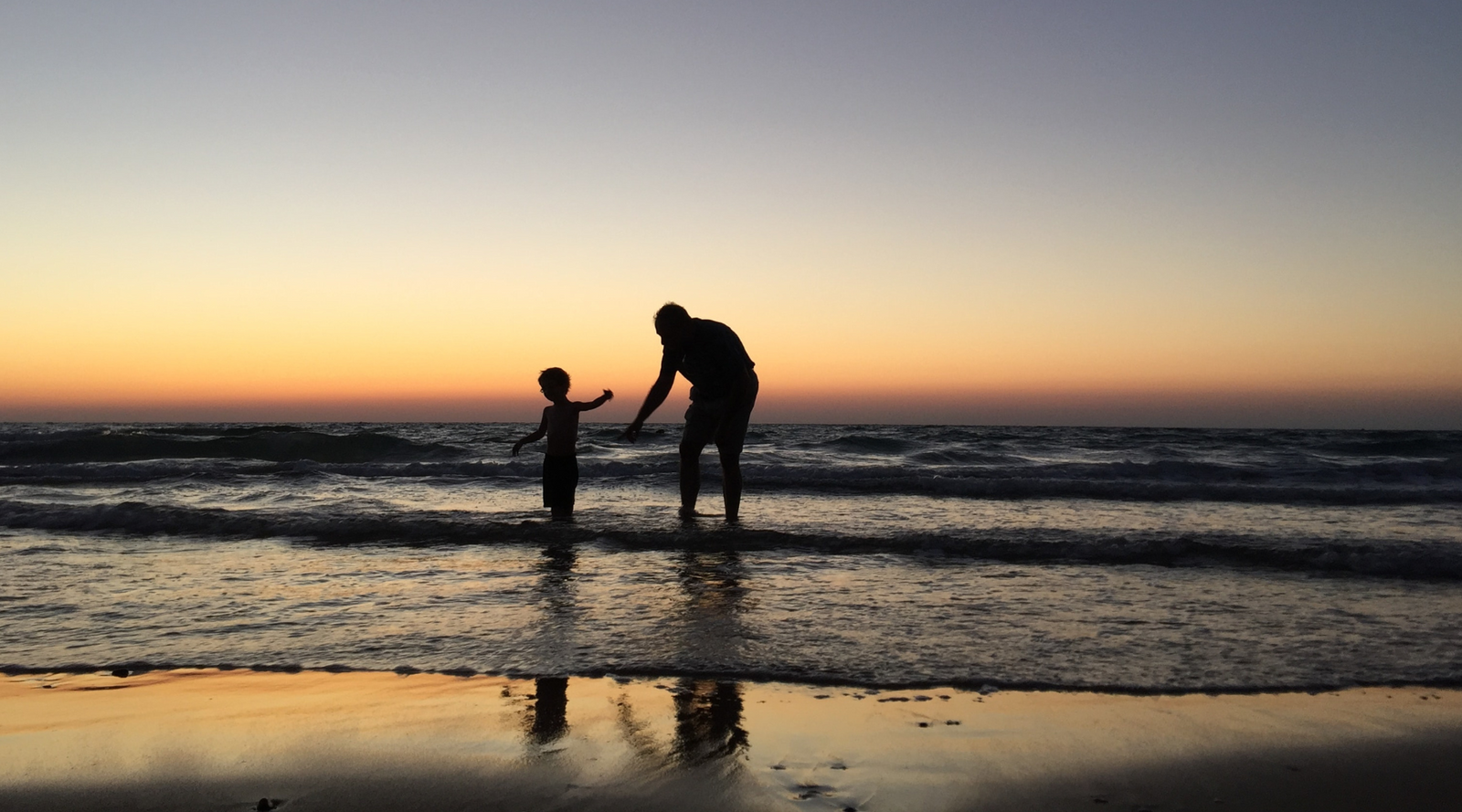 Silhouette of parent and child playing on the beach with sunset in the background.