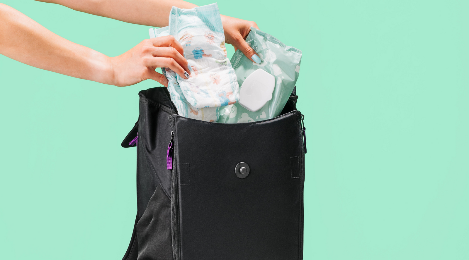 Hands packing baby wipes into black backpack against a teal background.