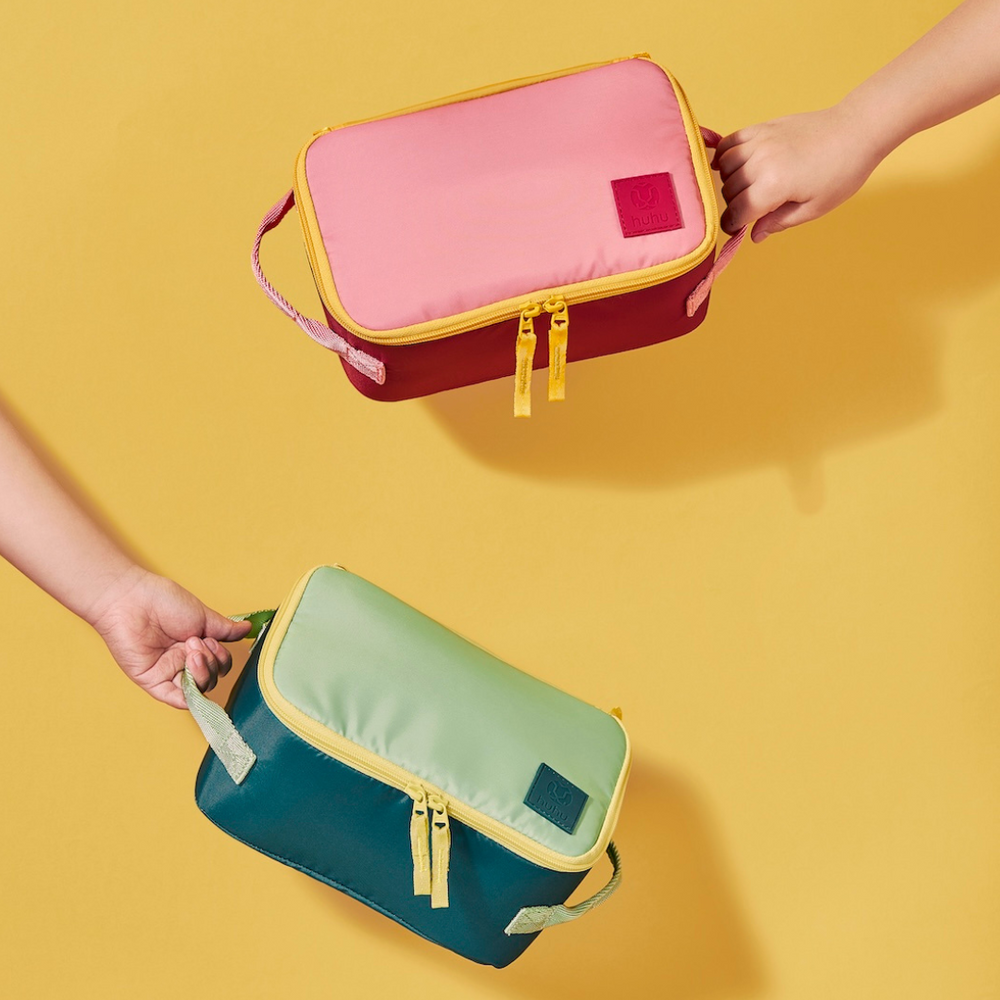 One hand holding pink and yellow insulated cooler bag and another hand holding green and yellow insulated cooler bag against a yellow background.
