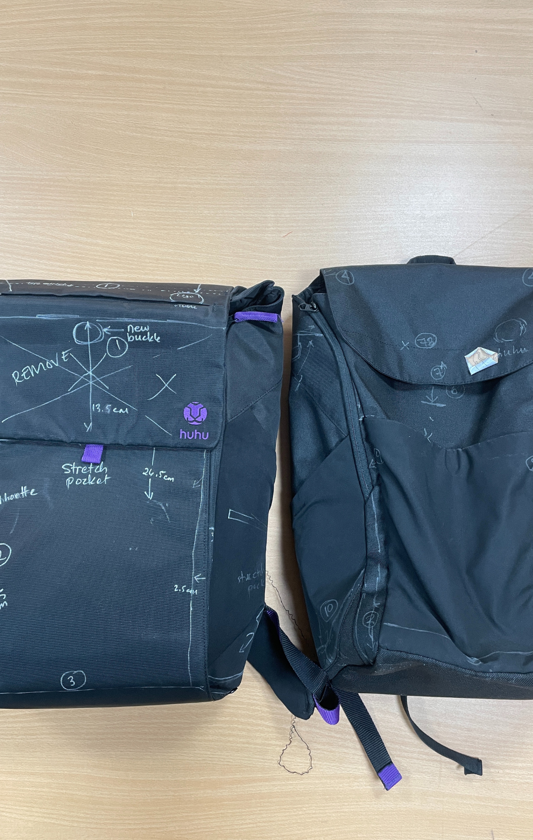 Black backpack sample on wooden surface with white chalk markups of production corrections to be made.