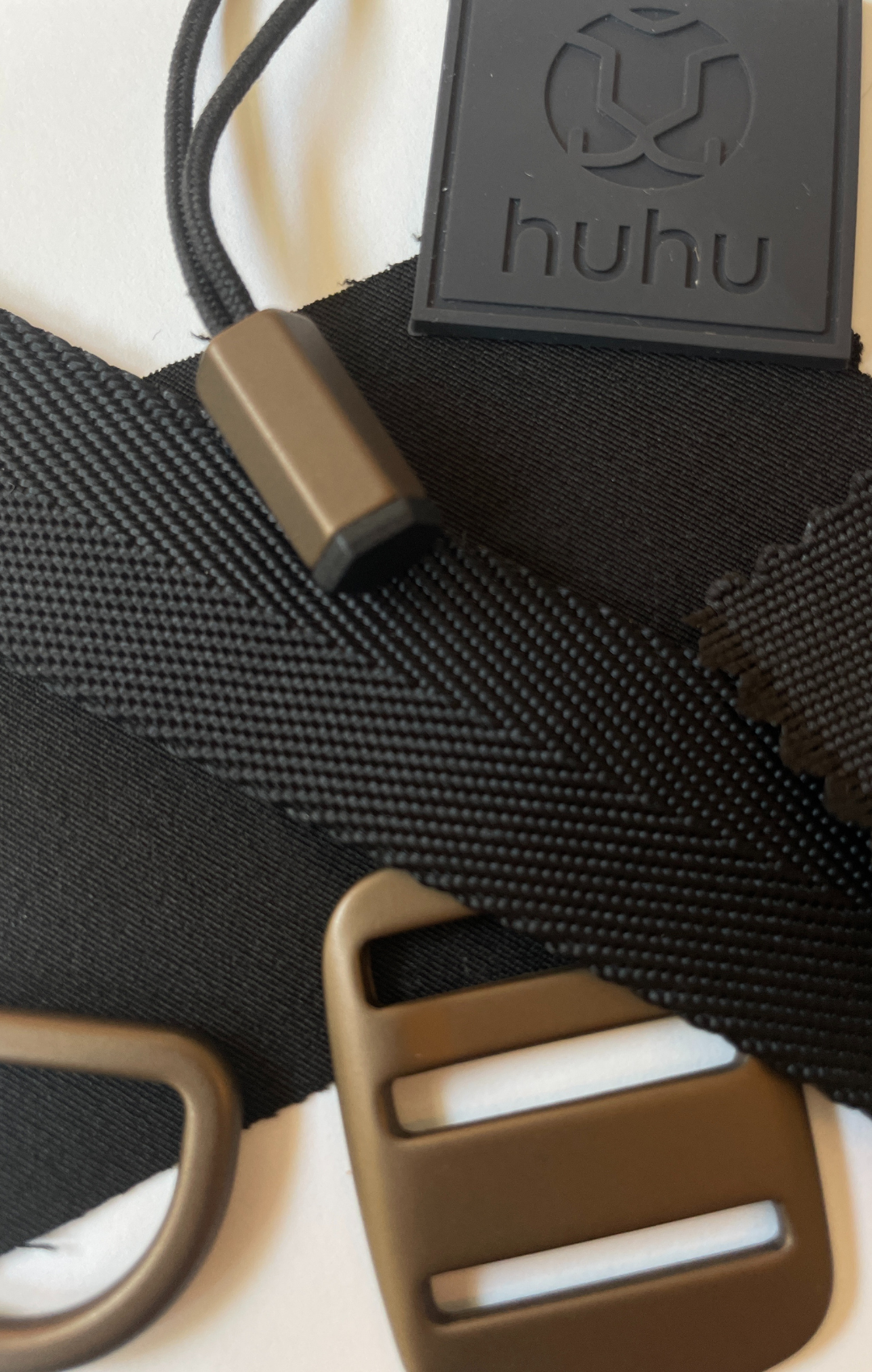 Close up of black fabric, Huhu logo, and strap samples with gold hardware for backpack.