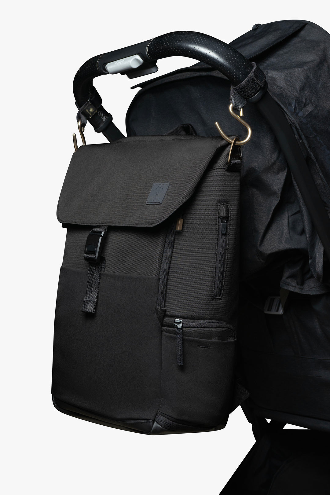 Black backpack hanging by gold stroller hooks on handle of black stroller against a white background.