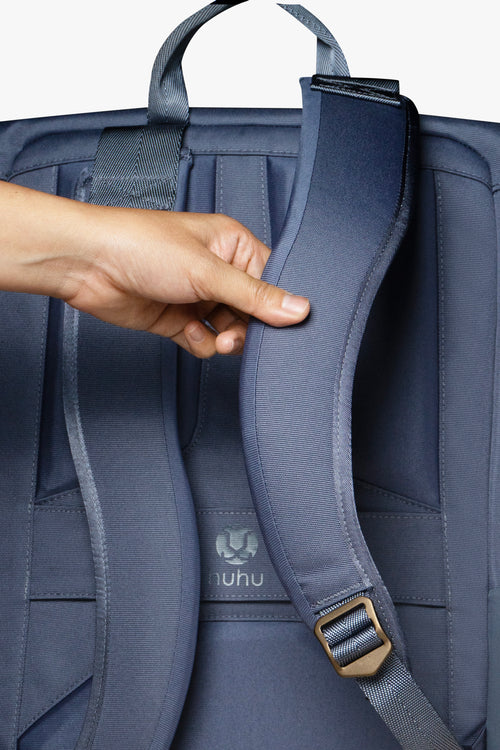 Back view of blue backpack against white background. Hand is touching padded strap of backpack.