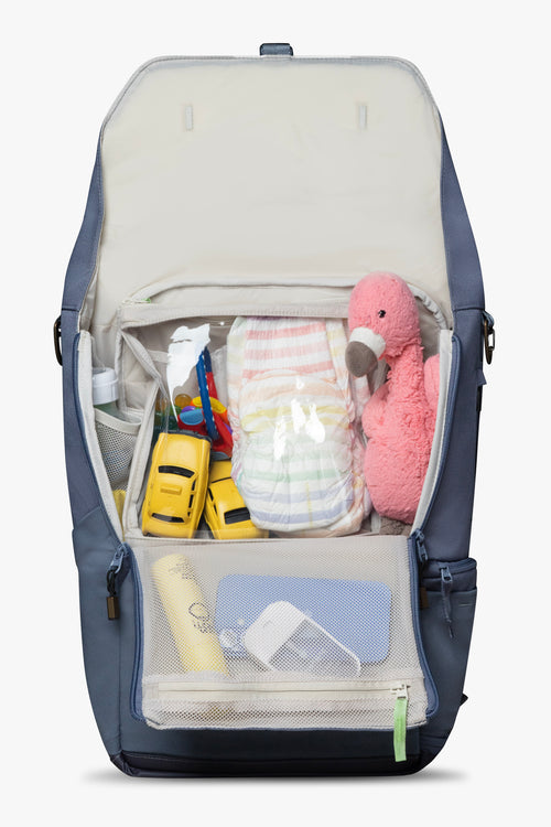 Front view blue backpack opened to reveal beige interior with beige packing pouch. Backpack and packing pouch are packed with brightly colored children's items. White background.