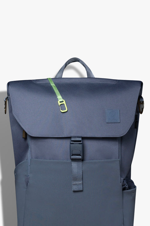 Front view of blue backpack against white background. Green key hook is hanging out from the zipper pocket on top of the backpack.