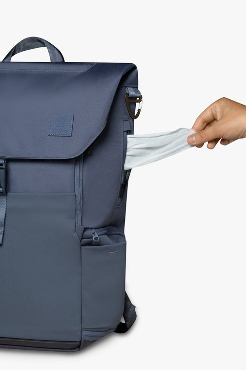 Front view of blue backpack with hand pulling wipe from exterior wipes pocket on side of backpack.