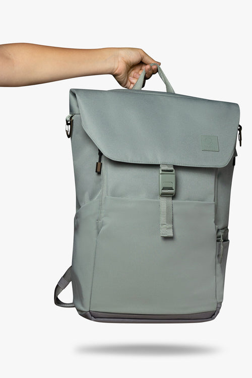 Hand holding green backpack by its top handle against white background.