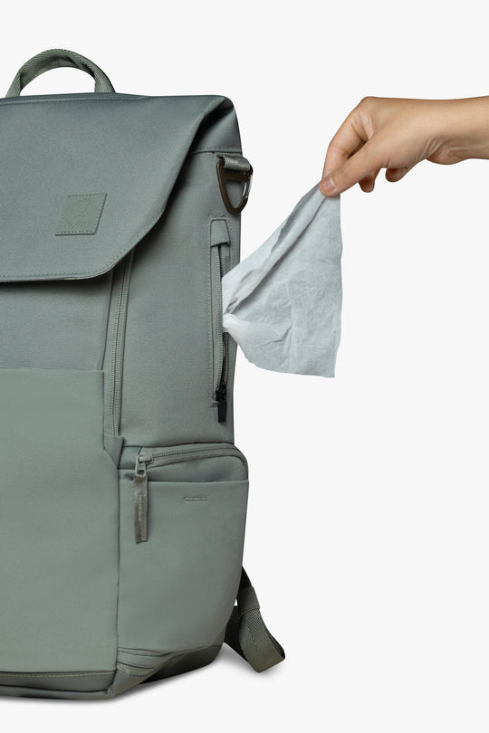 Front view of green backpack with hand pulling wipe from exterior wipes pocket on side of backpack.