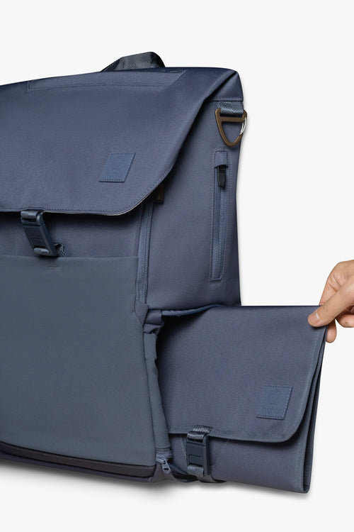 Hand sliding blue changing wallet into side locker pocket of blue backpack against white background.