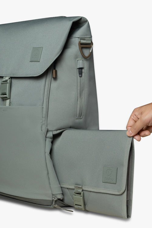 Hand sliding green changing wallet into side locker pocket of green backpack against white background.