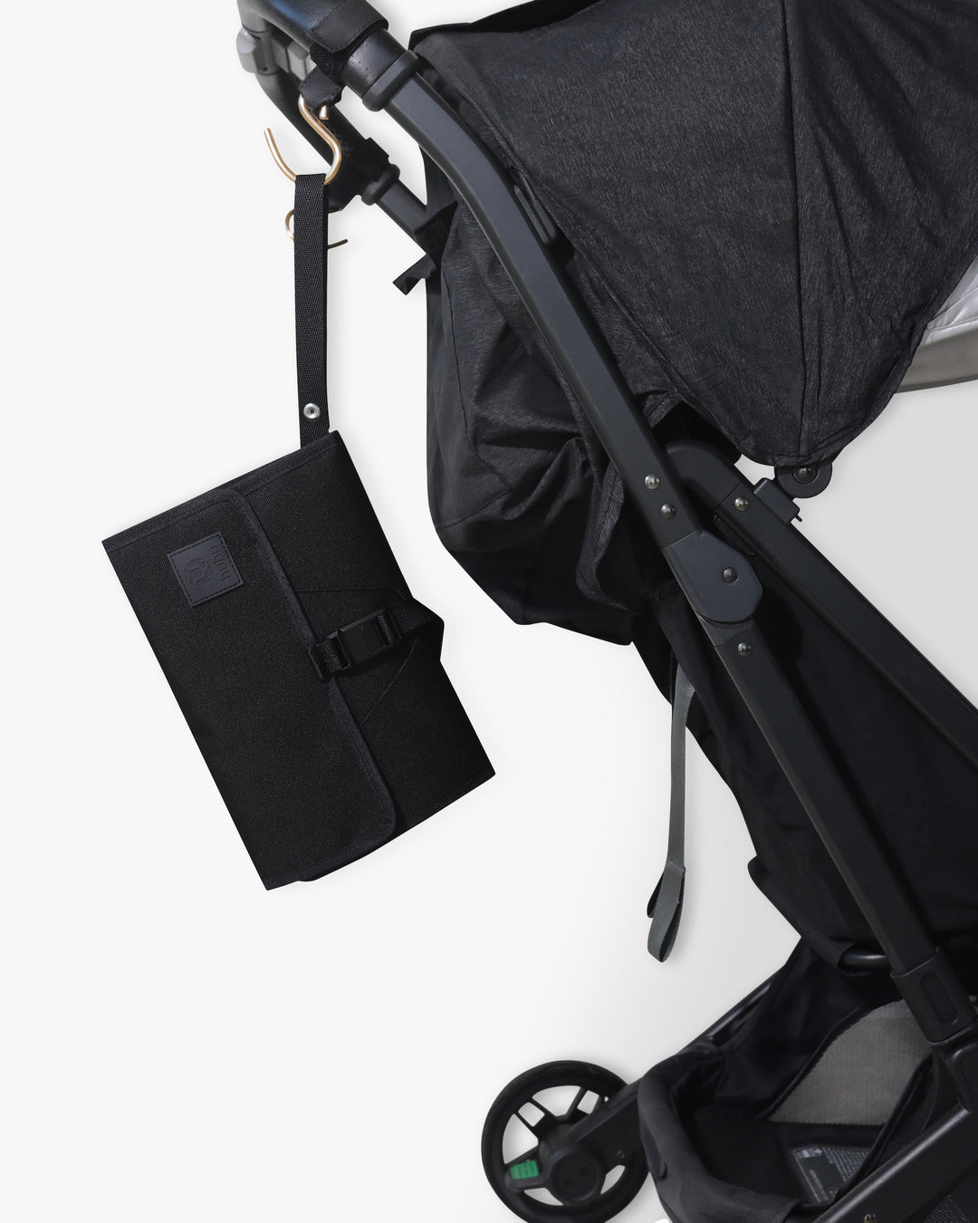 Black changing wallet with strap hanging from stroller hook on a black stroller against a white background.