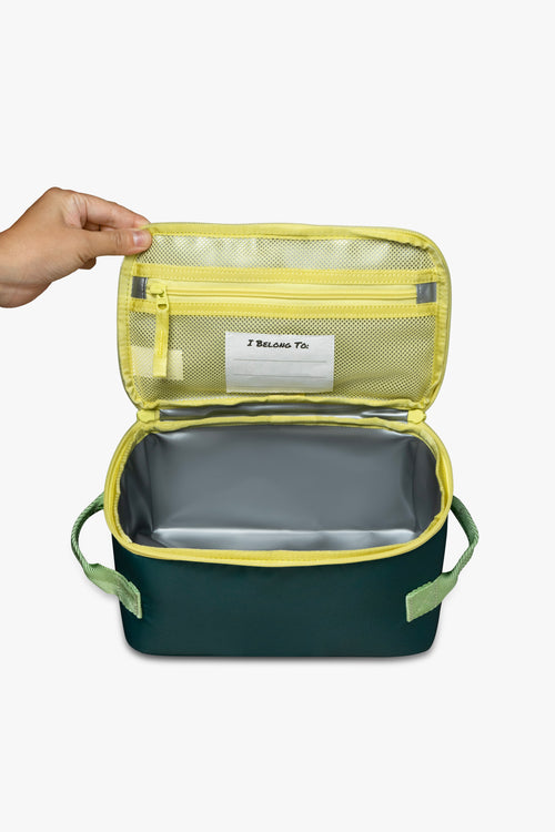 Front view of hand opening green insulated cooler bag to reveal yellow mesh zippered pocket, white "I belong to" tag, and silver interior against a white background.