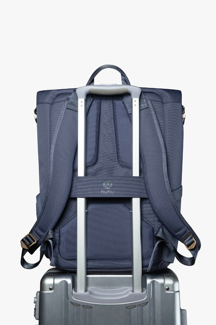 Blue backpack with luggage strap over rolling suitcase handle.