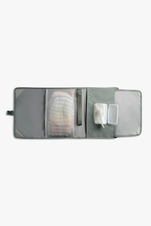 Front view of horizontal opened green changing wallet with taupe interior against a white background. Shows diapers in a taupe mesh pocket, a green strap, and wipes in a designated wipes pocket.