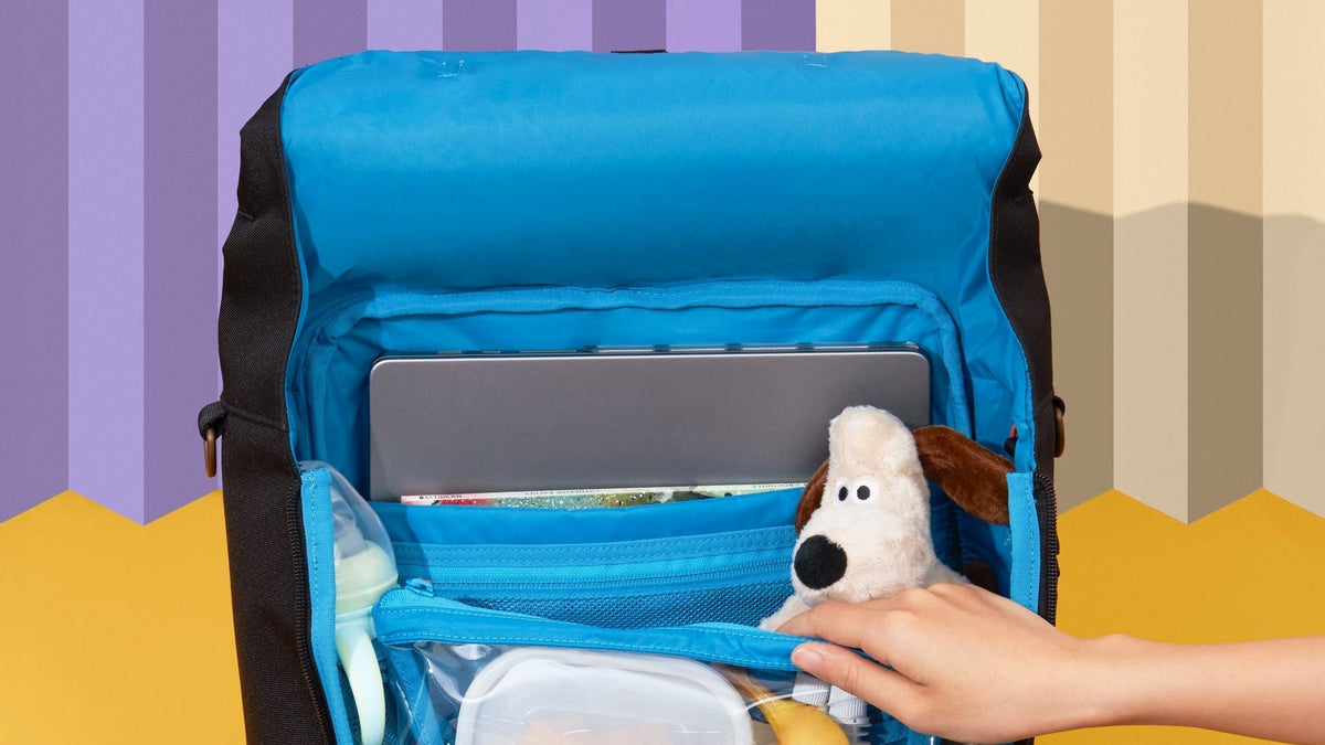The open Huhu Everyday Diaper Backpack with a laptop in its padded pocket above a bottle and snacks.