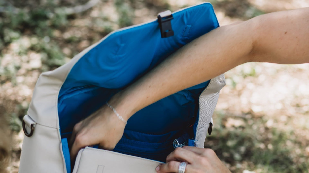 A hand reaches into a wide-open Huhu diaper backpack with a bright blue interior.
