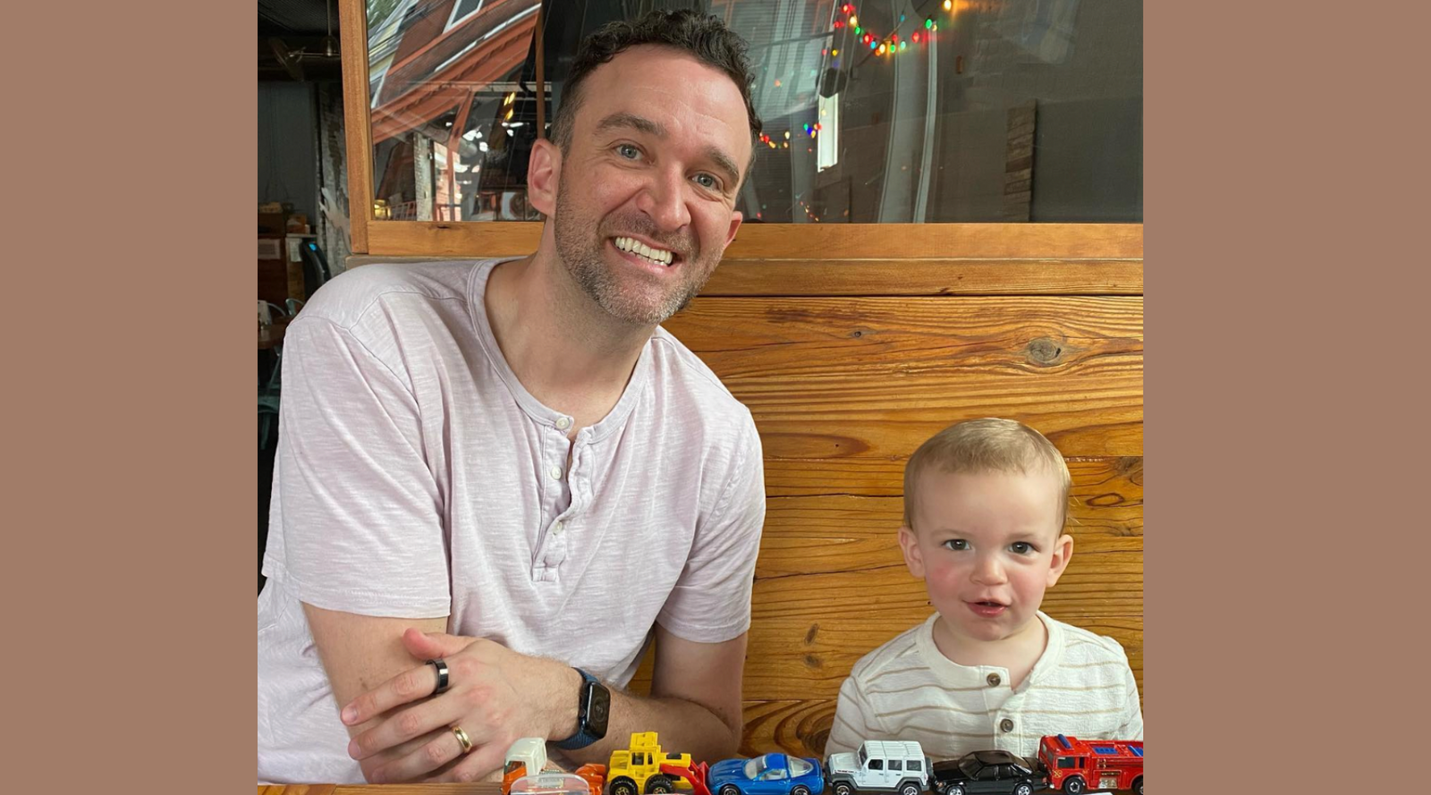 Dad sitting next to little boy. Both smiling at the camera.