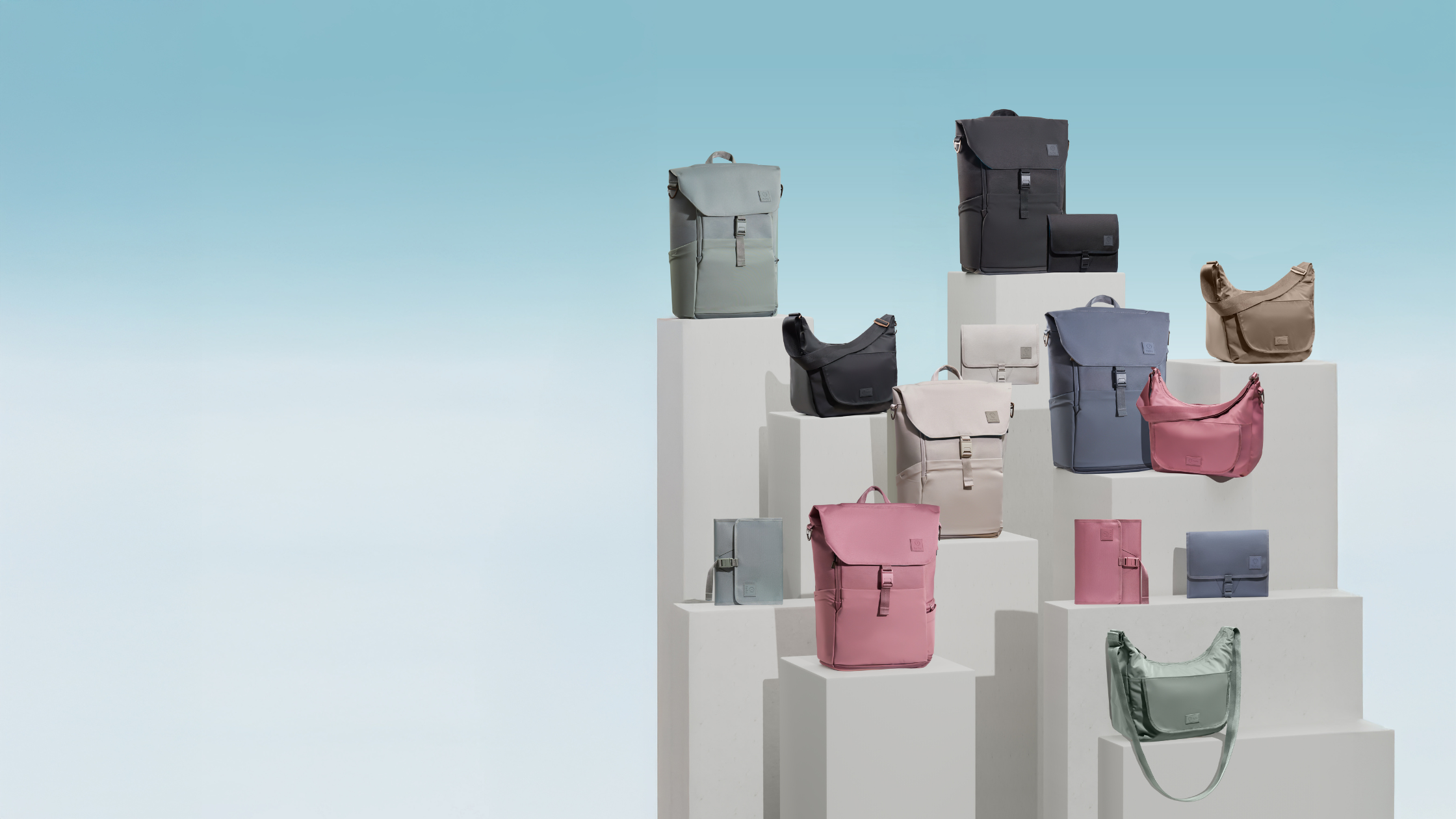 Diaper backpacks, crossbody diaper bags, and changing wallets arranged on pillars against blue background.