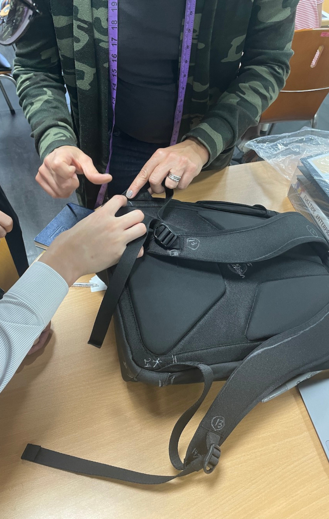 Close up of two people working on production corrections to be made on black backpack.