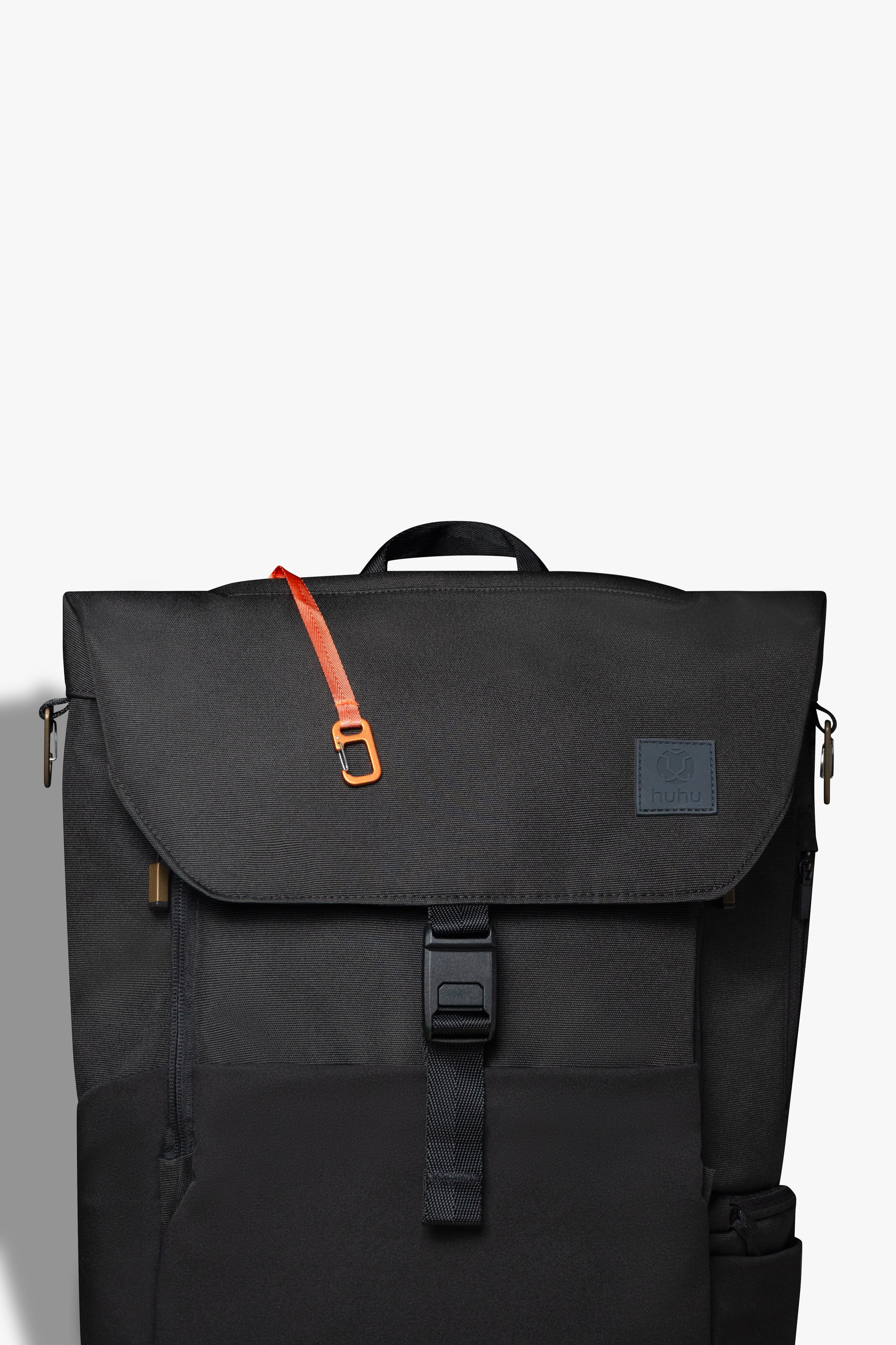 Front view of black backpack against white background. Orange key hook is hanging out from the zipper pocket on top of the backpack.