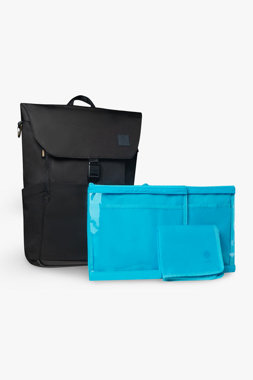 Front view of black backpack, closed and standing upright with 2 blue packing pouches and 1 blue folded changing pad against white background.