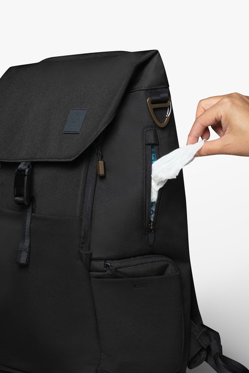 Front view of black backpack with hand pulling wipe from exterior wipes pocket on side of backpack.