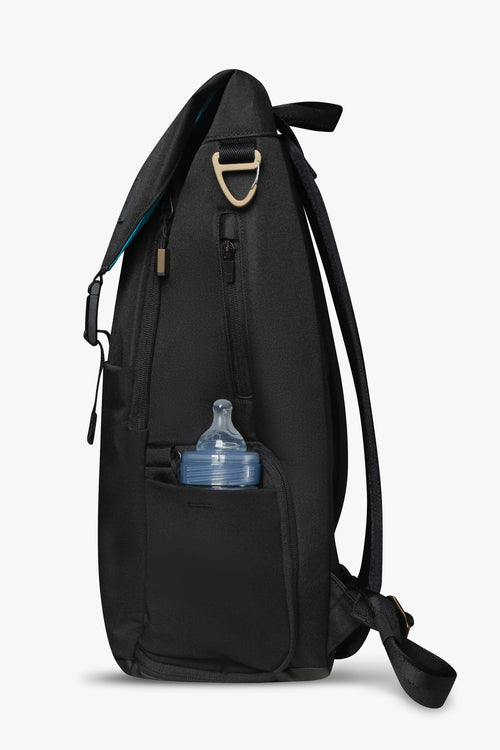 Side view of black backpack against a white background. Showing baby bottle in side stretchy bottle pocket. Bronze bag hardware and exterior zipper pocket are visible.
