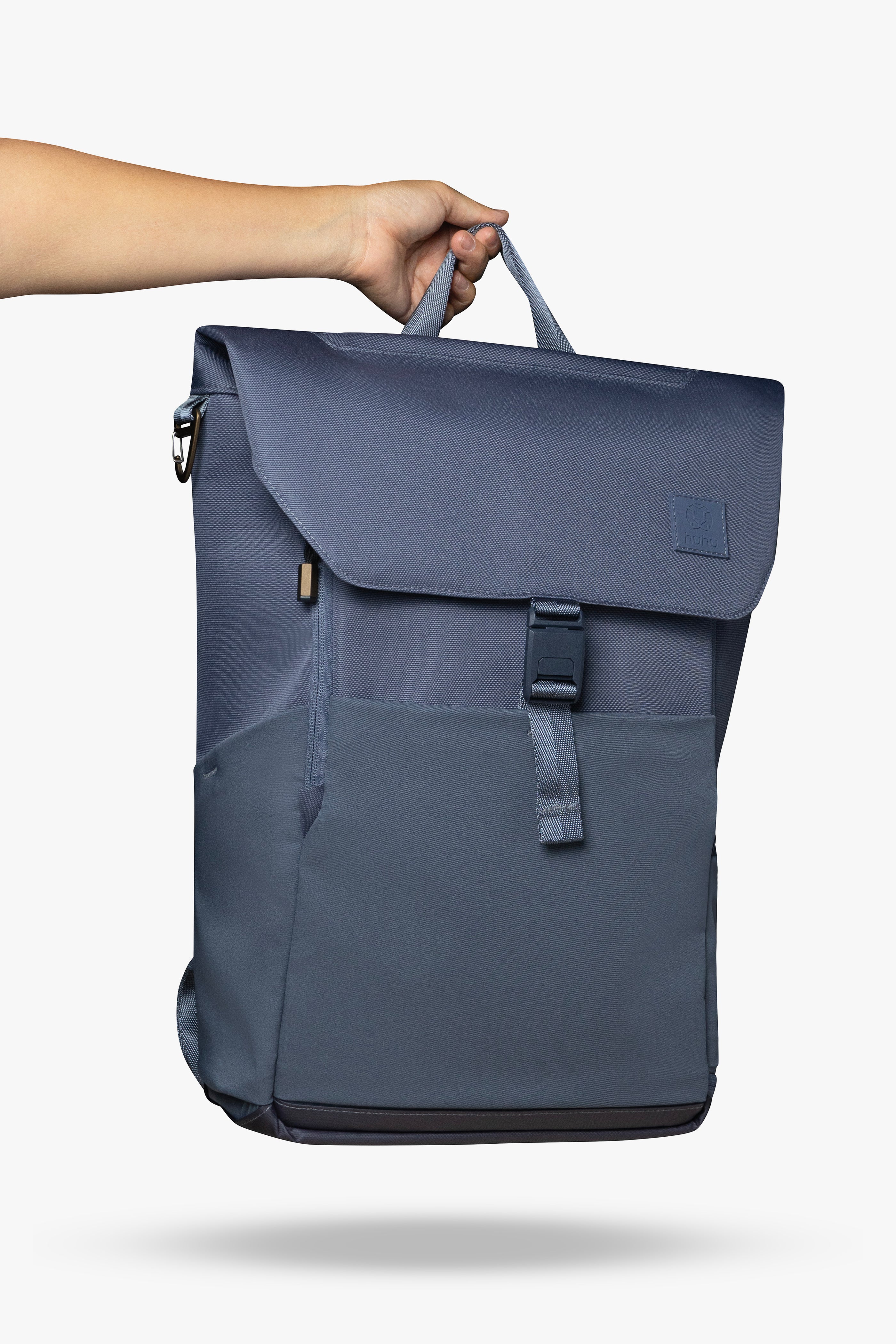Hand holding blue backpack by its top handle against white background.