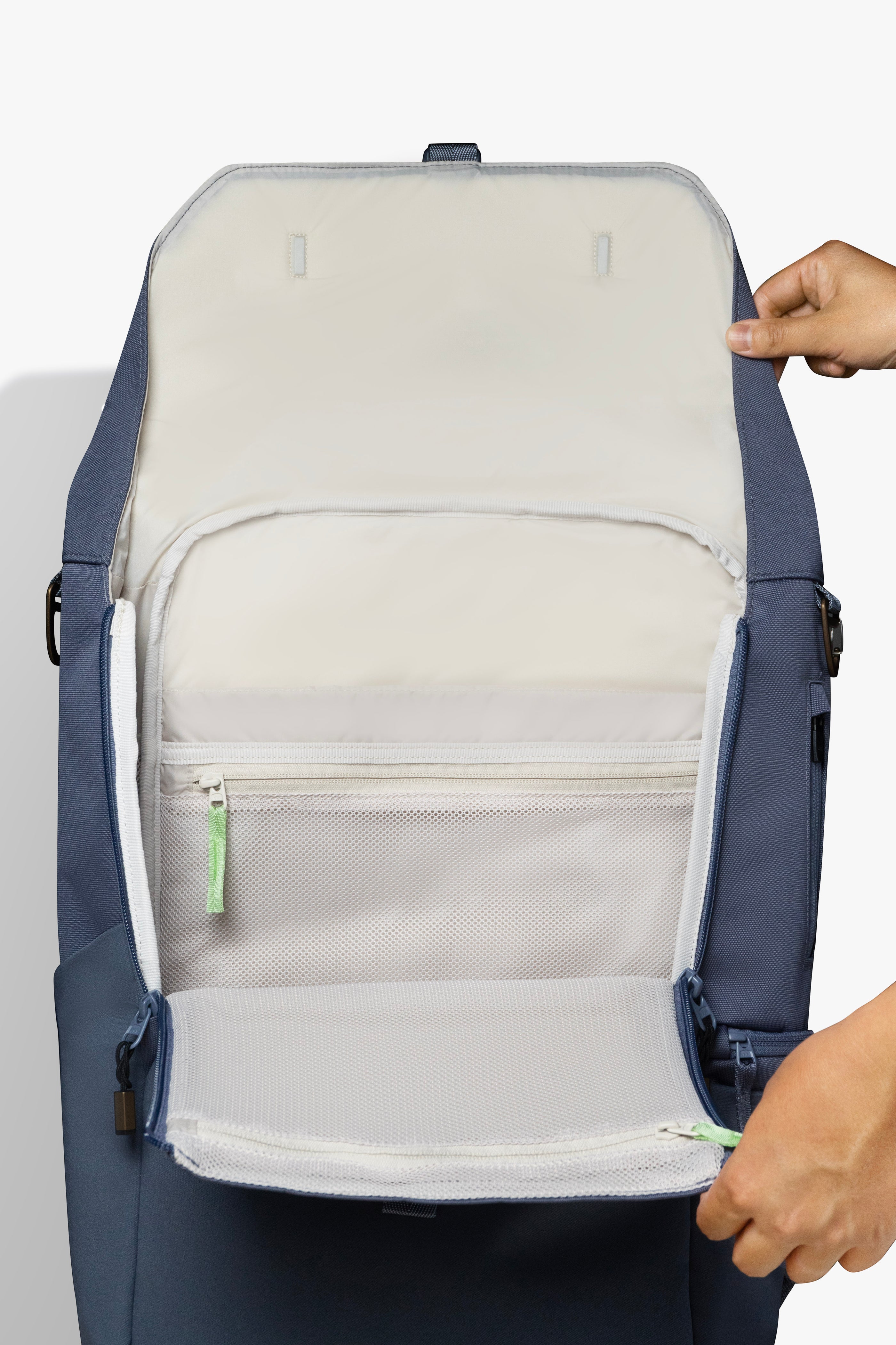 Front view of hands holding an opened blue backpack against white background. Image shows taupe interior of backpack and green zipper pull.