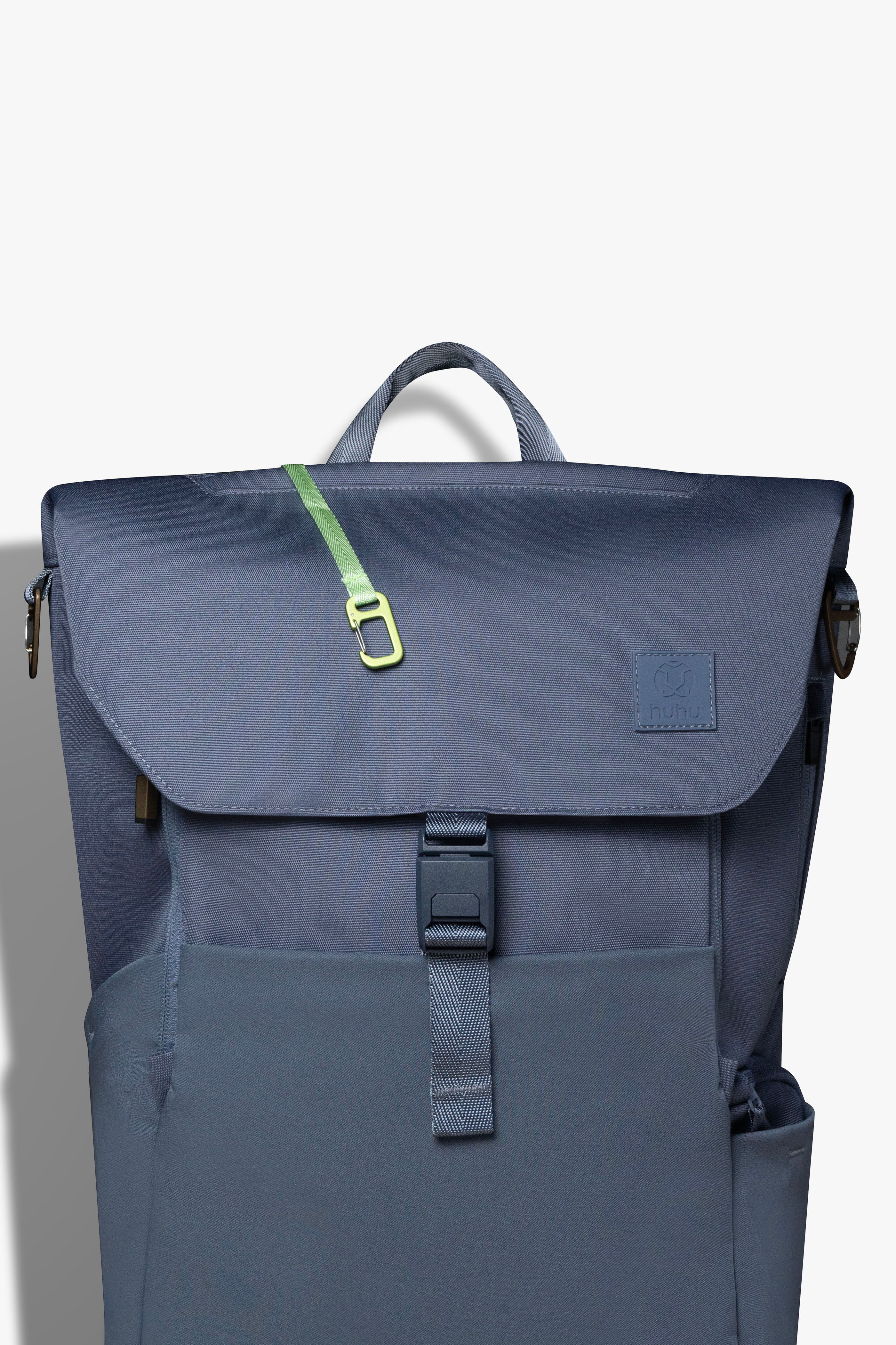 Front view of blue backpack against white background. Green key hook is hanging out from the zipper pocket on top of the backpack.