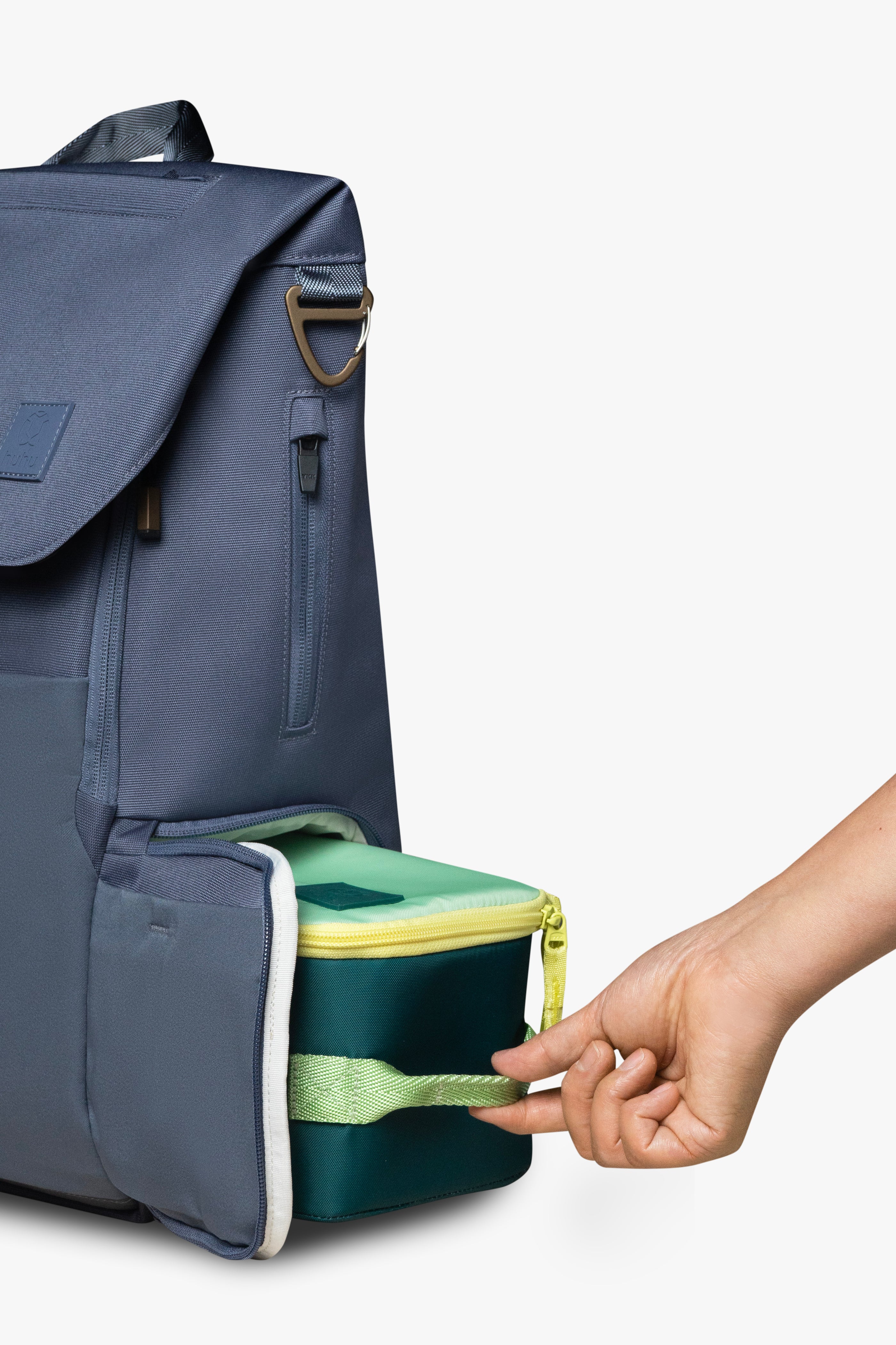Hand sliding green and yellow insulated cooler bag into side locker pocket of blue backpack against white background.