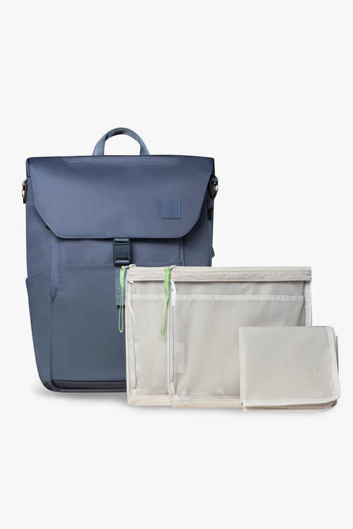 Front view of blue backpack, closed and standing upright with 2 taupe packing pouches and 1 blue folded changing pad against white background.