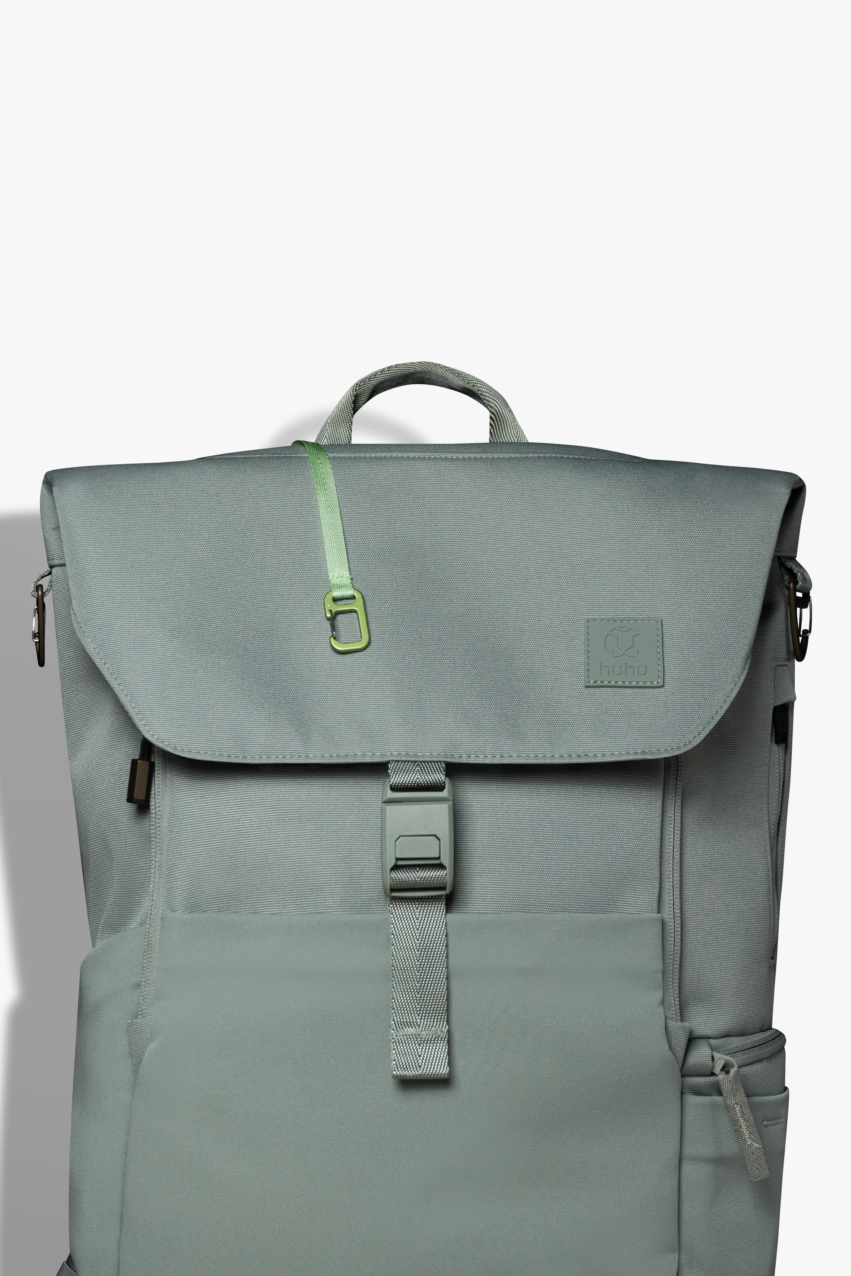 Front view of green backpack against white background. Green key hook is hanging out from the zipper pocket on top of the backpack.
