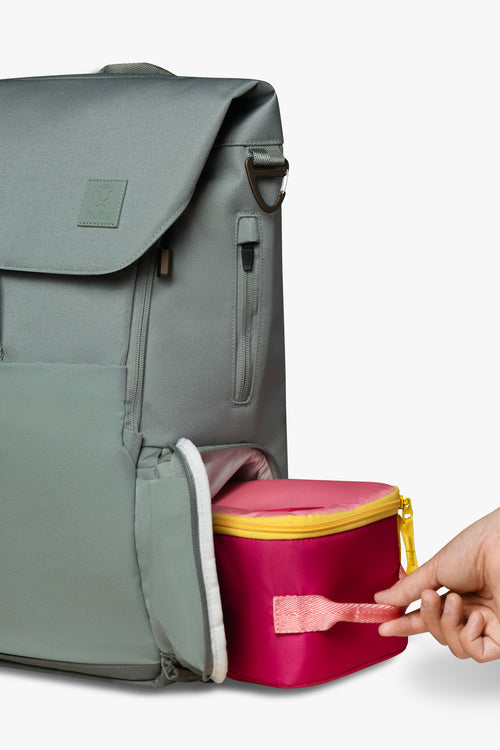 Hand sliding pink and yellow insulated cooler bag into side locker pocket of green backpack against white background.