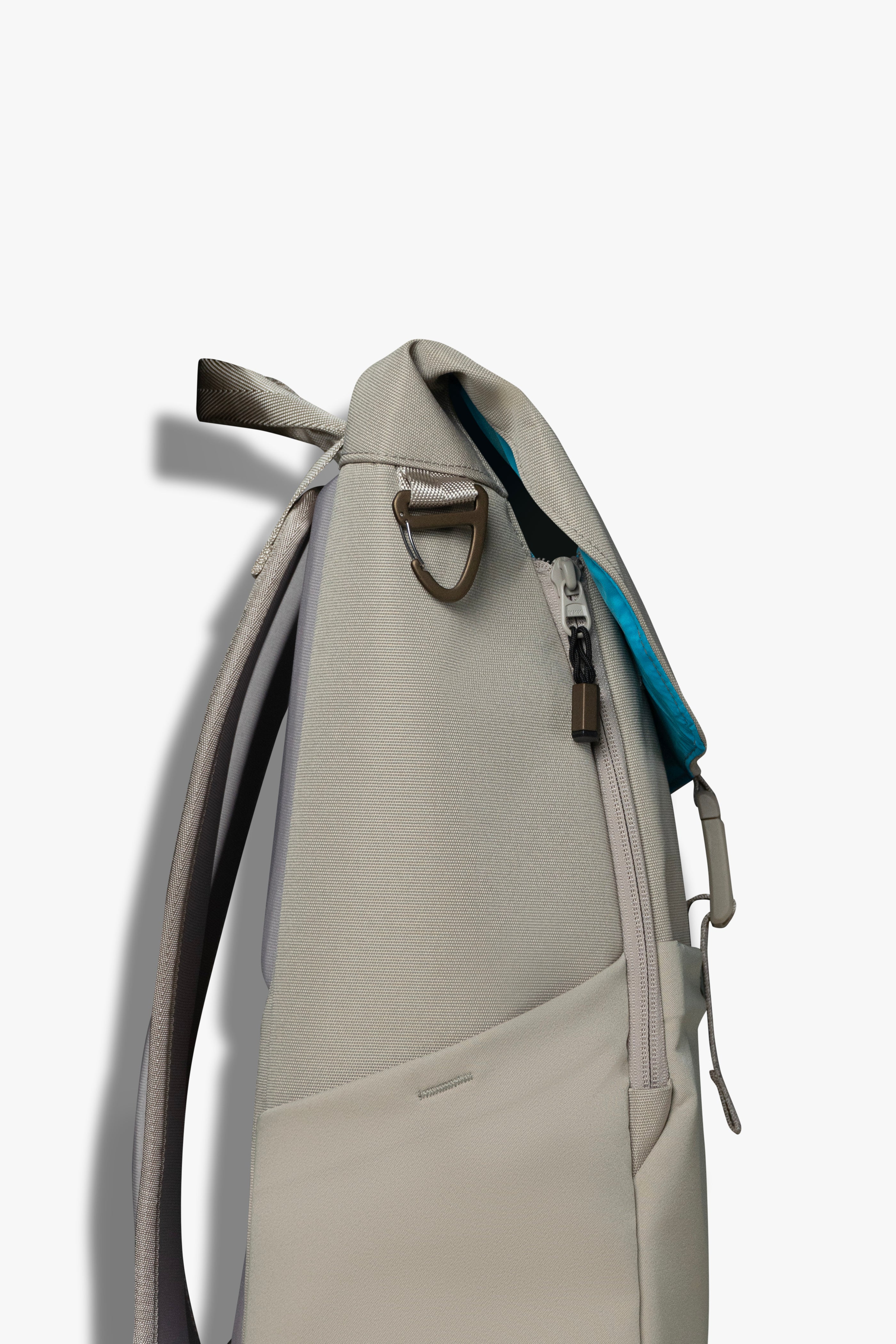 Side view of taupe backpack showing bronze carabiner clip hook.