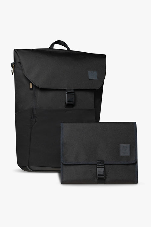 Front view of black backpack and changing wallet. Both are closed, and show magnetic clasp and exterior of products against white background.