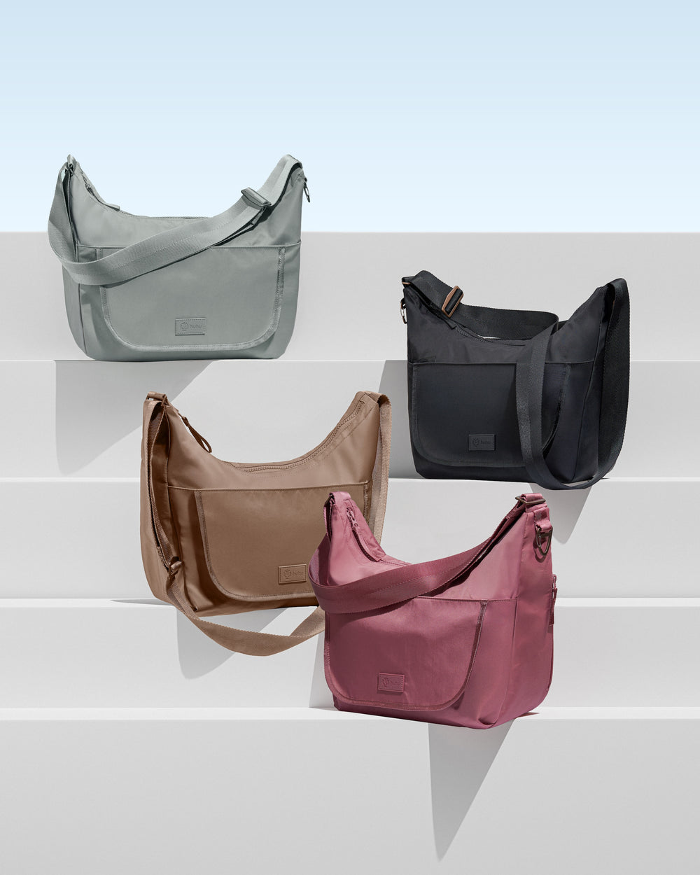 Four handbags in gray, black, brown, and pink on a white surface with a light blue gradient background.