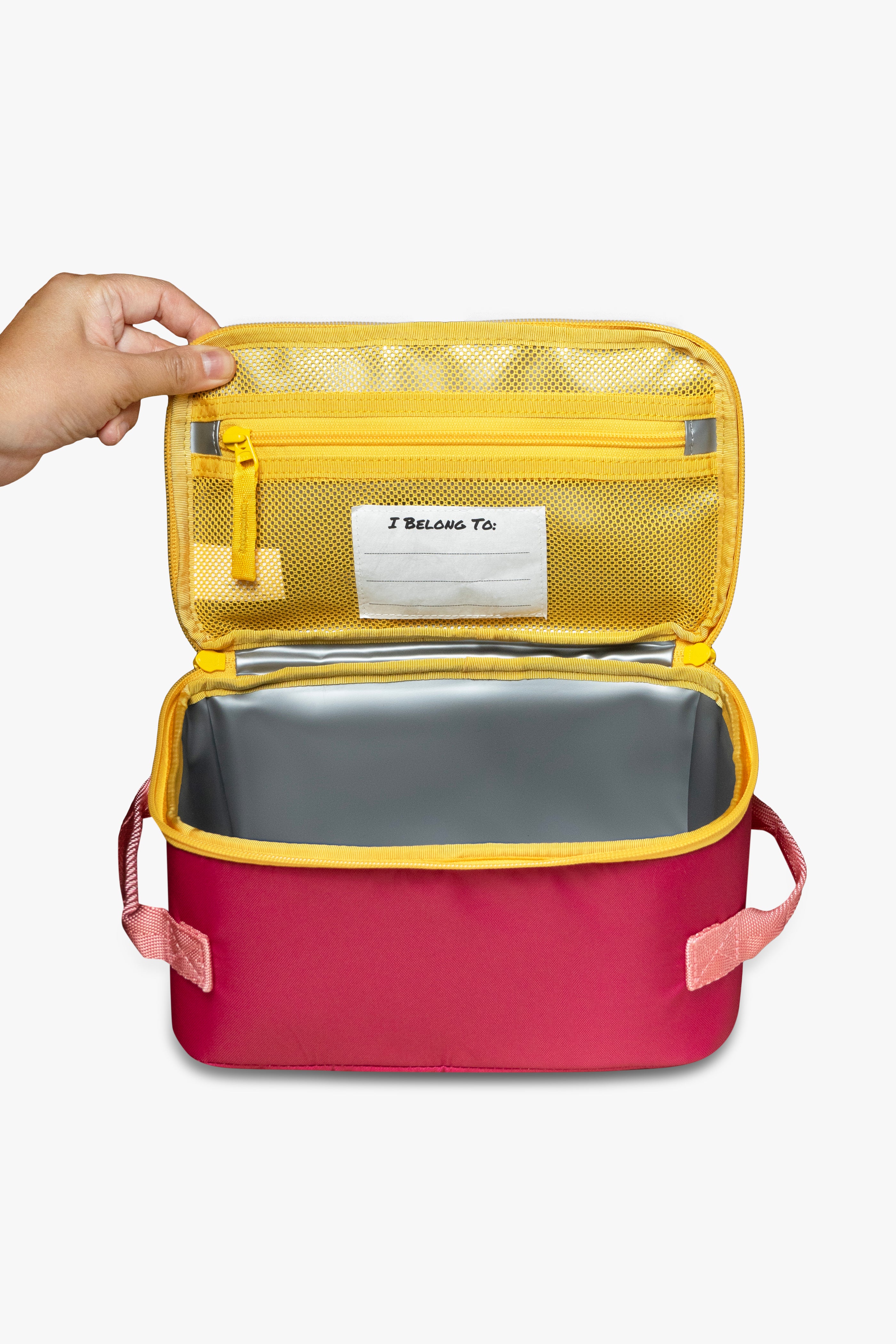 Front view of hand opening pink insulated cooler bag to reveal yellow mesh zippered pocket, white "I belong to" tag, and silver interior against a white background.