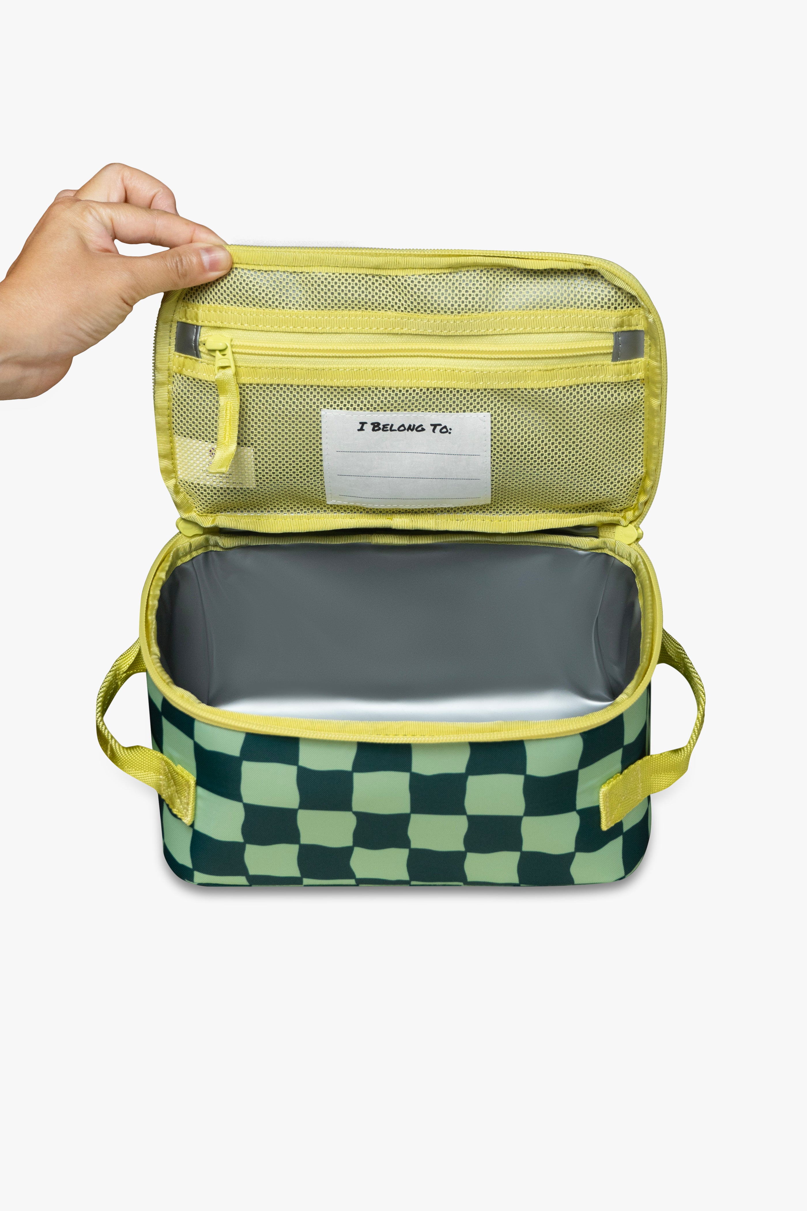 Front view of hand opening green checkered insulated cooler bag to reveal yellow mesh zippered pocket, white "I belong to" tag, and silver interior against a white background.