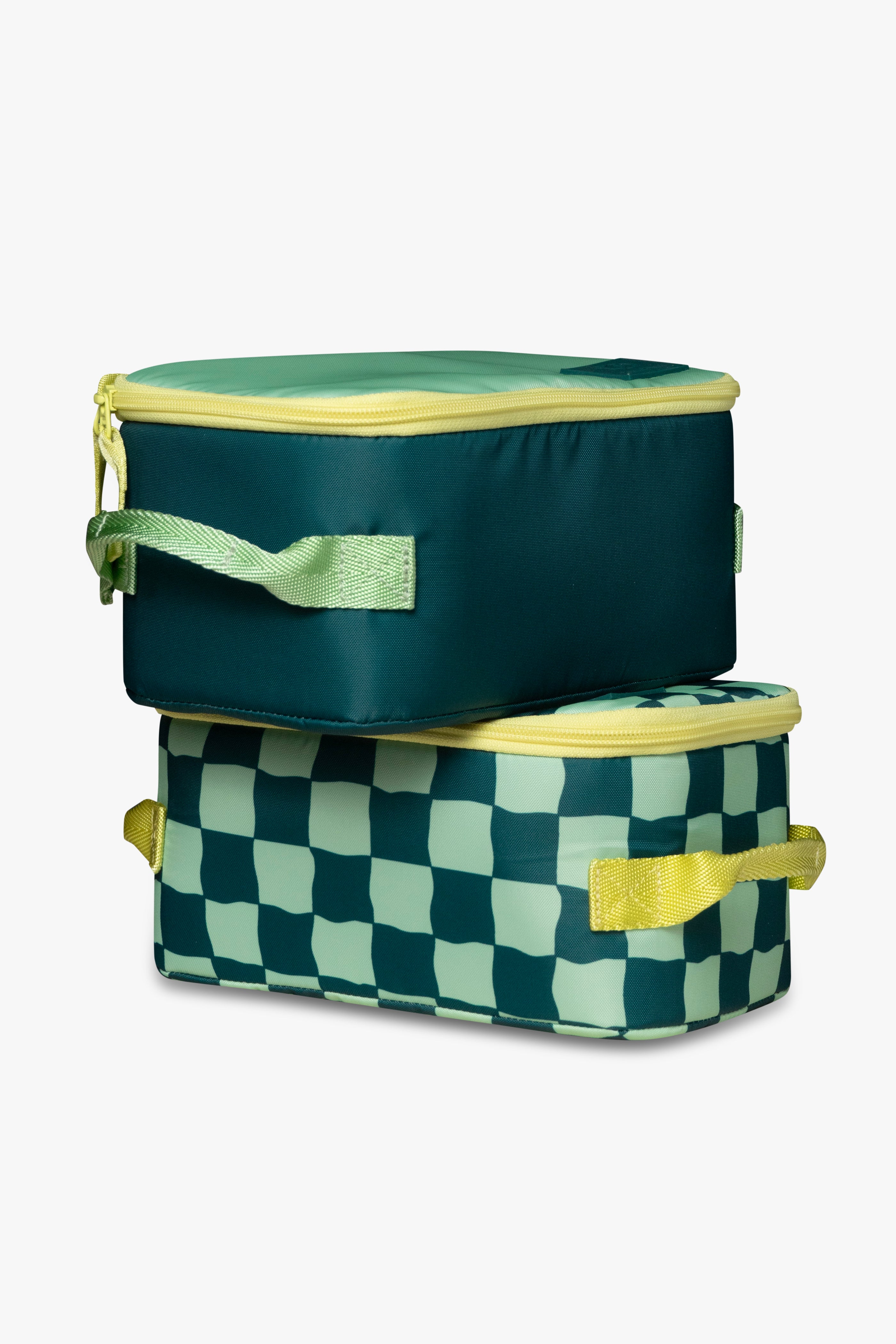 Solid green insulated cooler bag with yellow zipper sitting on top of green checkered insulated cooler bag with yellow zipper against a white background.