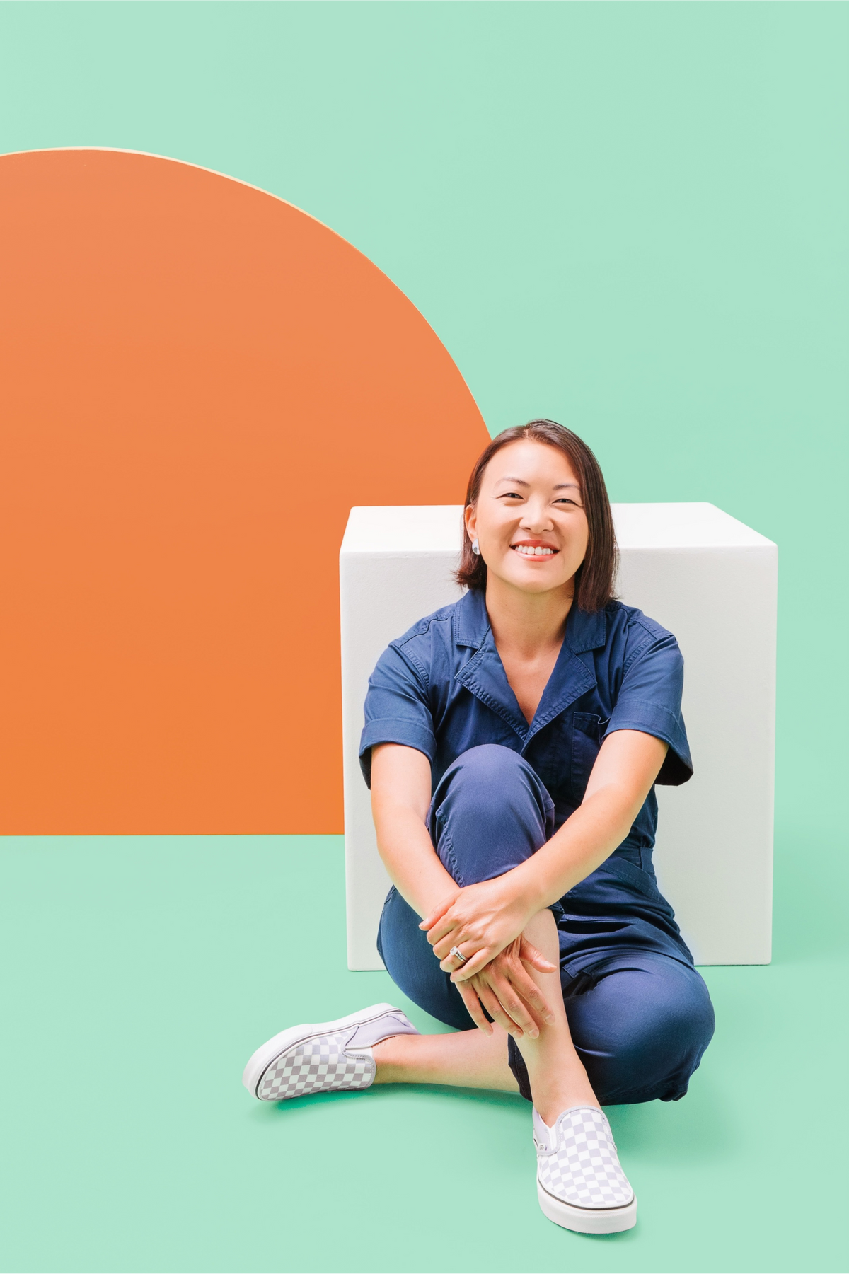 Woman sitting on a white chair against a colorful background with an orange arc and green wall.