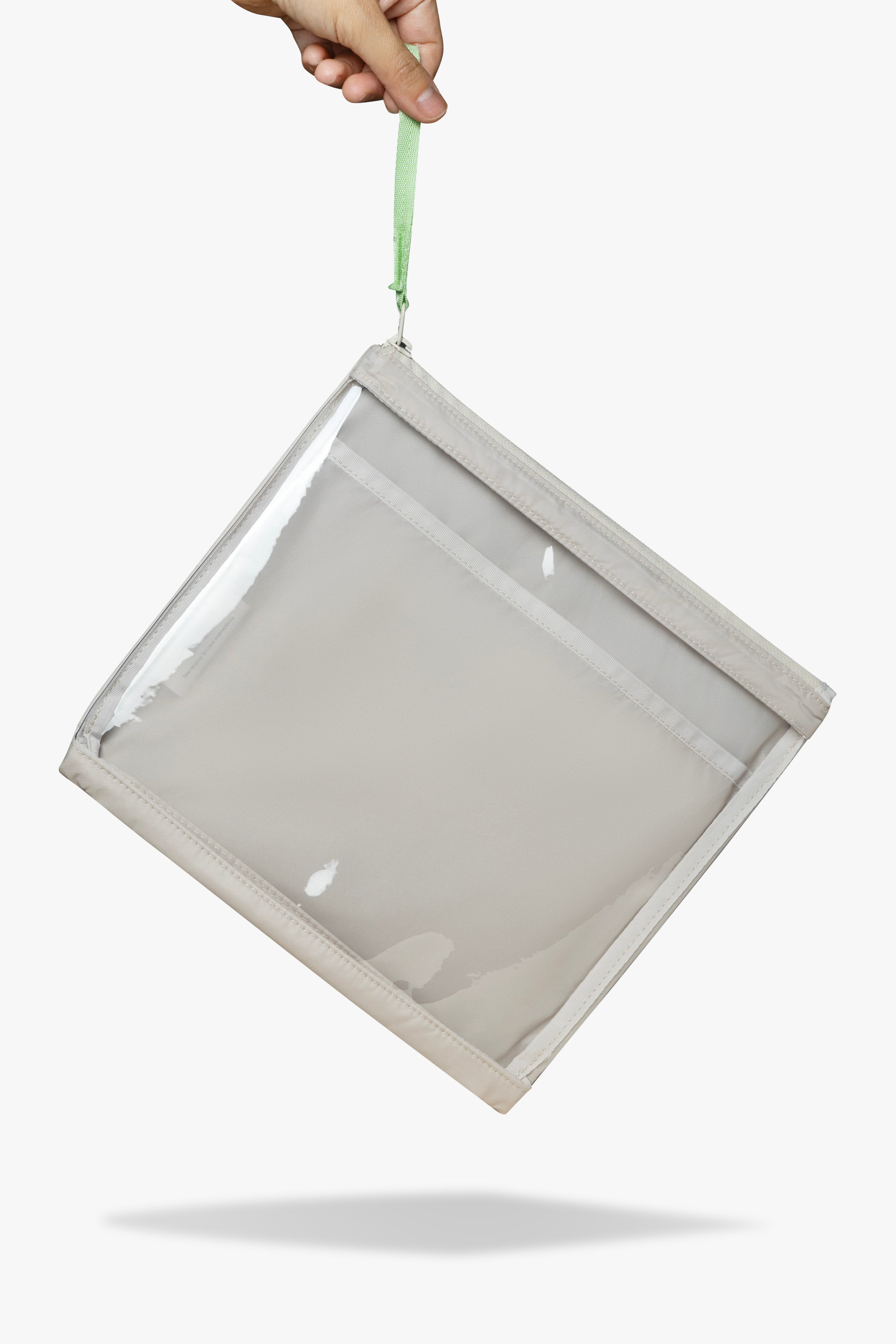 Front view of hand dangling beige changing wallet with clear front by its green zipper pull.