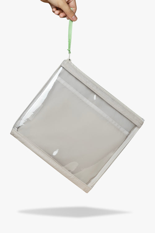 Front view of hand dangling beige changing wallet with clear front by its green zipper pull.