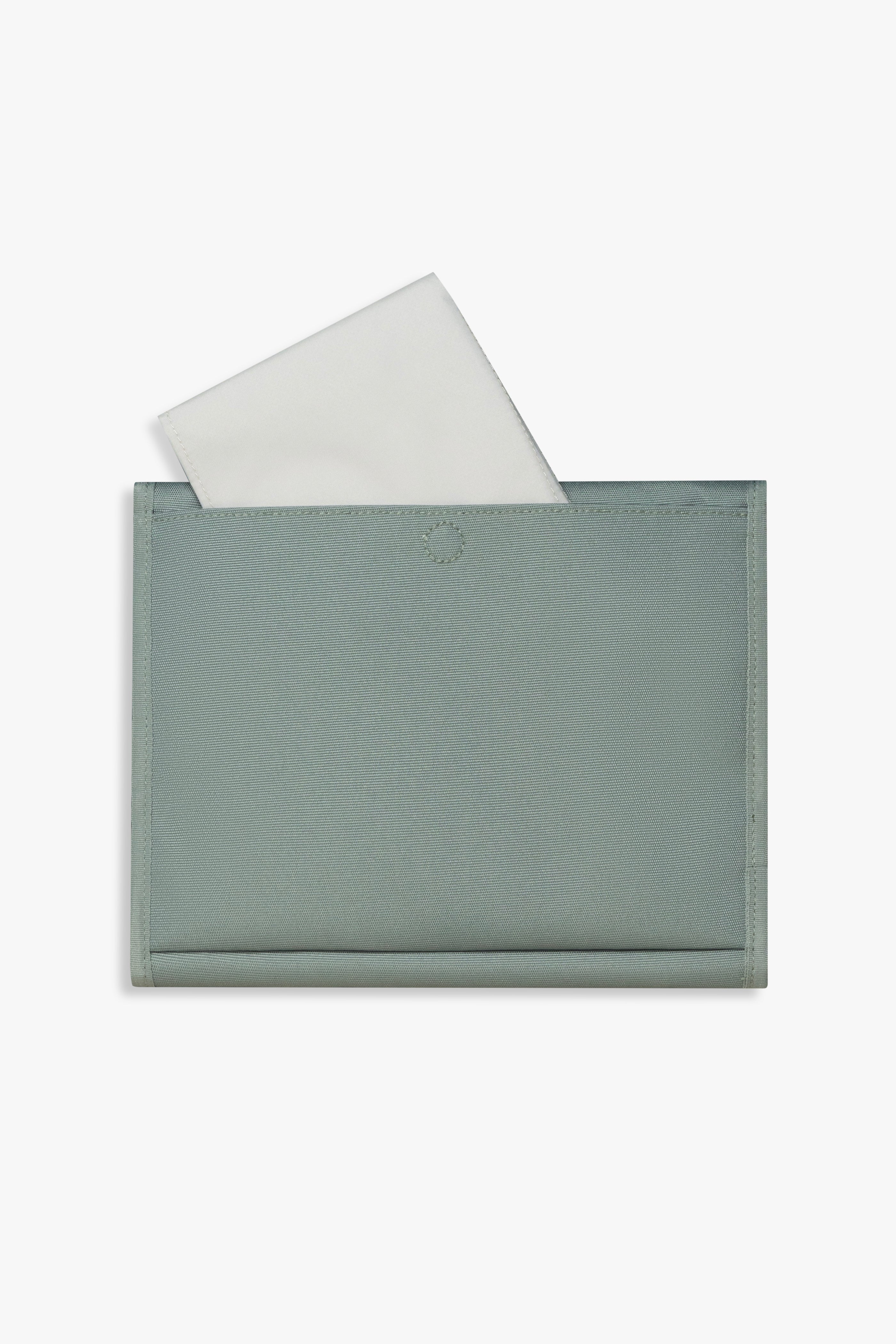 Back view of closed green changing wallet against a white background showing taupe changing pad sitting halfway out of back pocket.