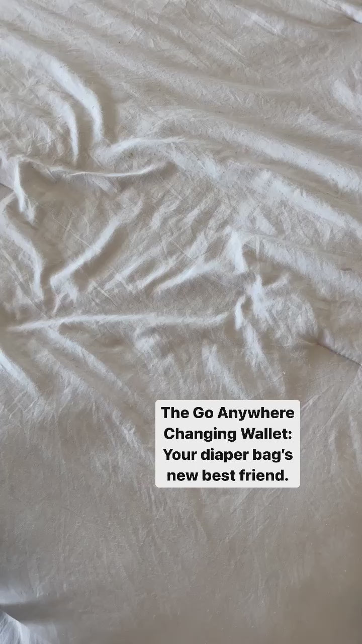 Video packing diapers and wipes into a black changing wallet with a blue interior, against a beige background.